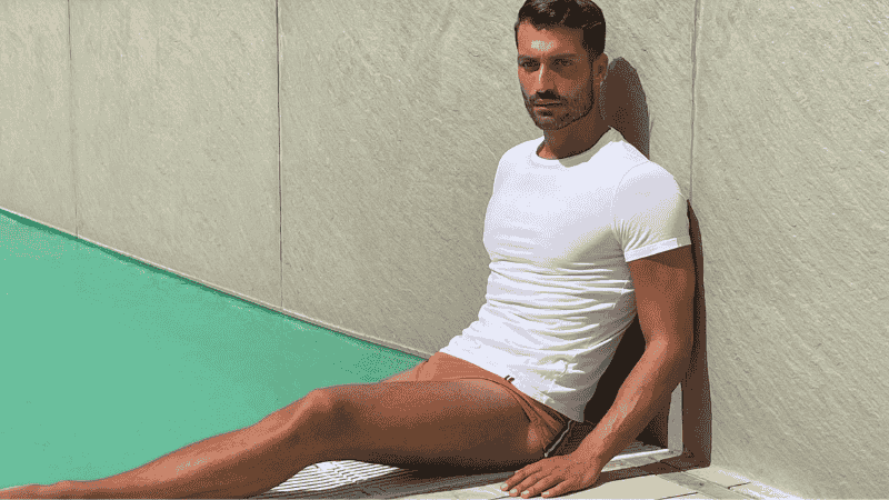male model sitting against the wall on edge of the swimming pool outdoor